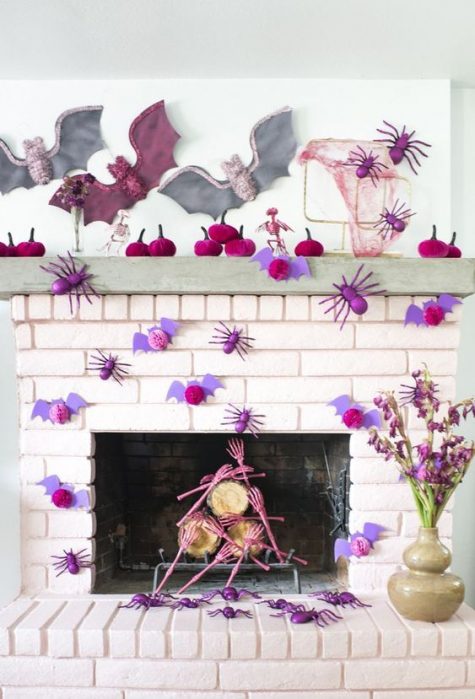 a bright pink Halloween mantel with lots of paper spiders, bats, pumpkins and skeleton hands