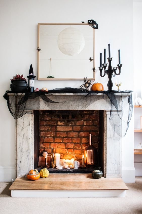 a chic Halloween mantel with candles, bottles, a witch hat, black tulle, natural pumpkins and blooms in a cauldron