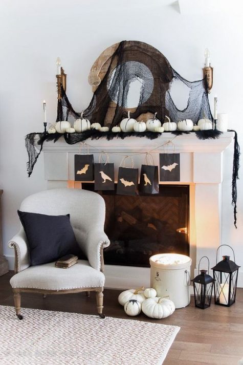 a monochromatic Halloween mantel with black tulle, feathers, white pumpkins and candles