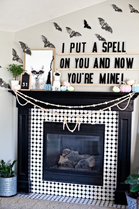 a whimsy Halloween mantel with bats on the wall, pastel pumpkins, a funny artwork and some greenery