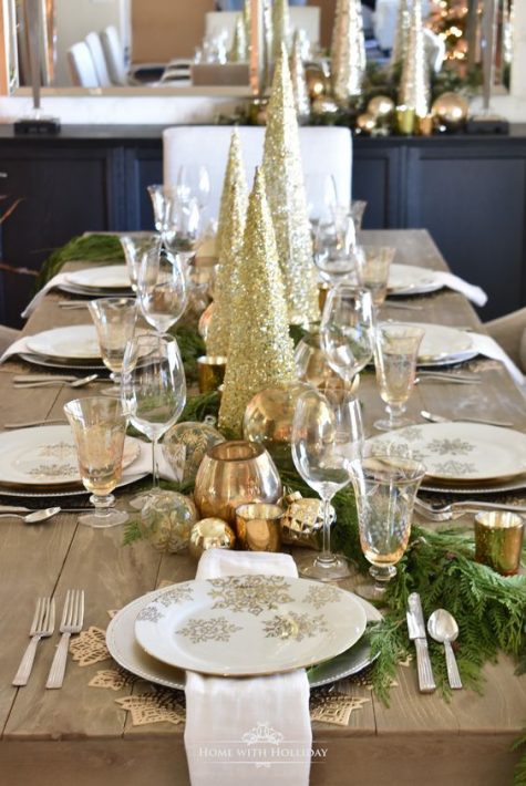 a stylish Christmas table with evergreens, gold snowflakes, placemats, gold glitter cone trees and gold ornaments and candleholders