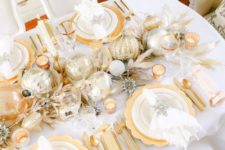 19 a shiny and bright gold and white Christmas table setting with gold chargers, metallic ornaments, branches, gold cutlery and silver elements