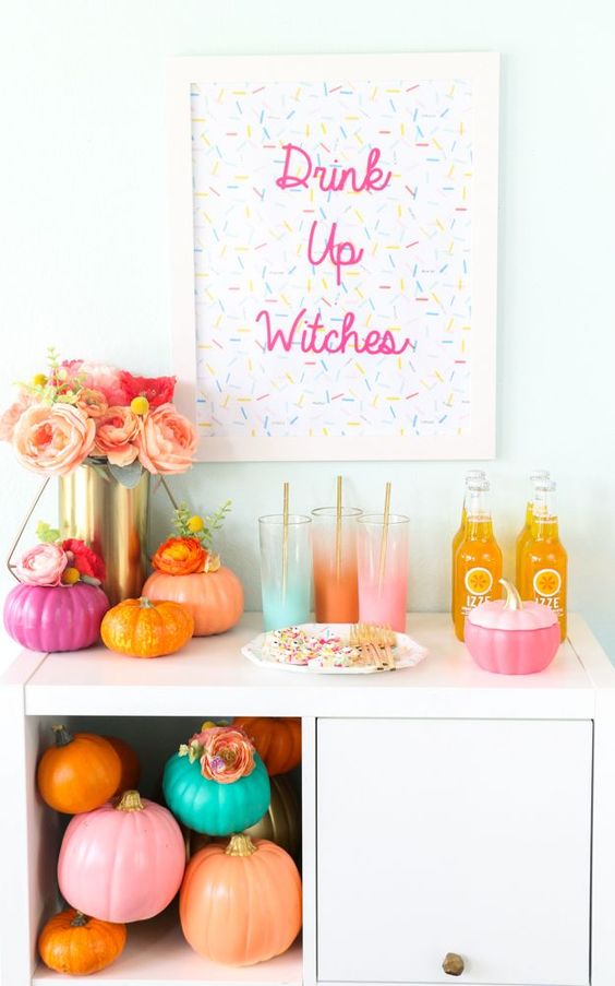a colorful Halloween drink bar with bright pumpkins, ombre glasses and a sprinkle sign, a lush floral centerpiece