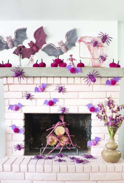 a colorful Halloween fireplace and mantel with fuchsia pumpkins, purple bats and spiders and skeleton hands in pink