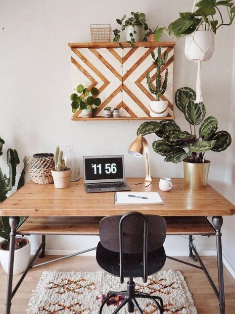 a boho home office nook with an industrial wood and metal desk, a black metal chair, a chevron shelving unit and potted plants