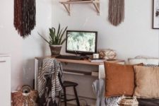 a boho home office with long fringe hanging, a sleek desk, lots of basket for storage and earthy tone pillows