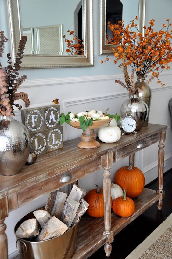 a bright Thanksgiving console table with white and orange pumpkins, dried eucalyptus and firewood