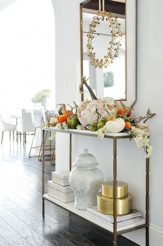 a chic console table with fake plastic and fabric pumpkins, white white blooms and a dried herb wreath over the table