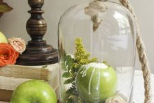 a cloche with rope and with greenery, ferns and a blush bloom inside plus a green apple as a candleholder