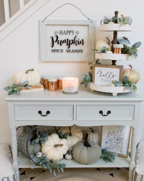 a cozy neutral Thanksgiving console table with lots of natural and faux pumpkins, greenery, candles and signs