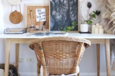 a cozy rustic meets boho home office nook with lot sof artworks, pampas grass, candles and a wicker chair