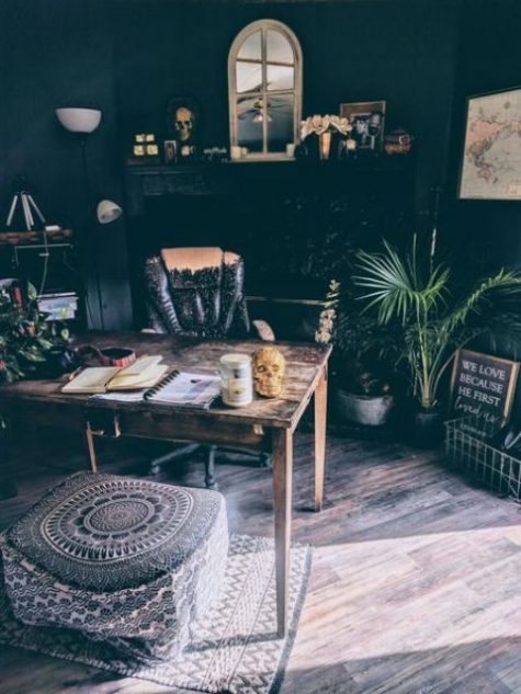 a moody boho home office with a vintage desk and chair, potted plants, a boho rug and ottoman