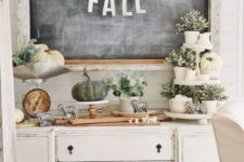 a neutral farmhouse console table with greenery in pots, white pumpkins, smal sheep figurines