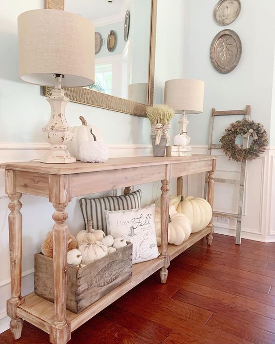 a neutral farmhouse console with white pumpkins, wheat, neutral pillows and a wooden crate