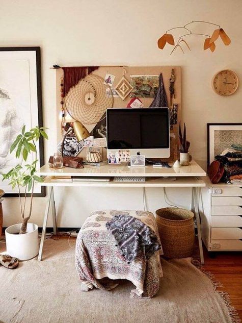 a relaxed boho office with a memo board with artworks, a boho stool and blanket, baskets and potted plants