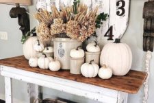 a rustic console table with white pumpkins, dried herbs, a vintage clock and a basket is a chic and cozy idea
