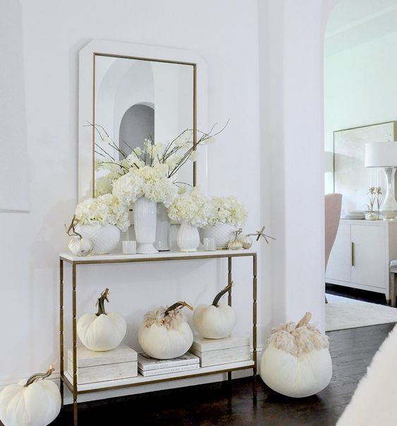 a simple and elegant Thanksgiving console with white blooms, pumpkins and white vases for a chic look