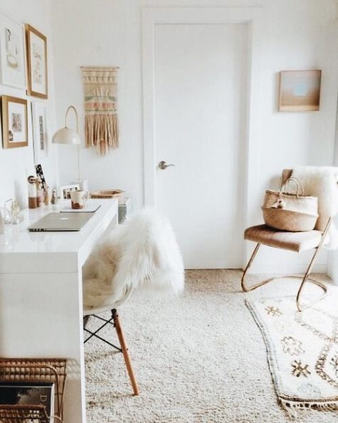a small and neutral boho home office with a macrame hanging, a leather chair, boho rugs, faux fur and a sleek white desk