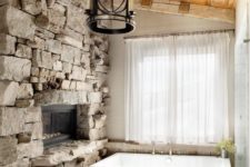 02 an attic bathroom with a rough stone wall with a fireplace, a pendant lamp and a wooden ceiling for a cozy feel
