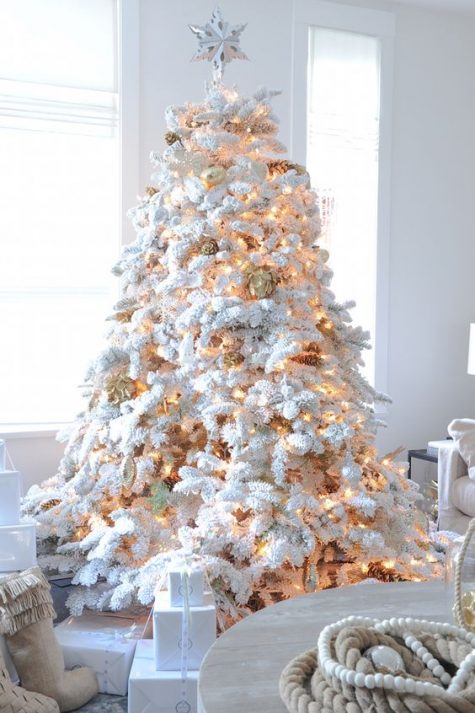 a flocked Christmas tree with lights and gilded pinecones looks like out of a fairy tale