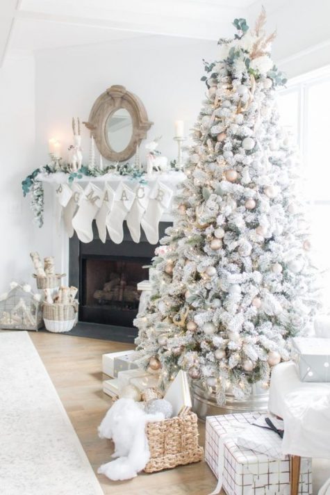 a beautiful flocked Christmas tree with lights and metallic and neutral ornaments plus fresh greenery on top
