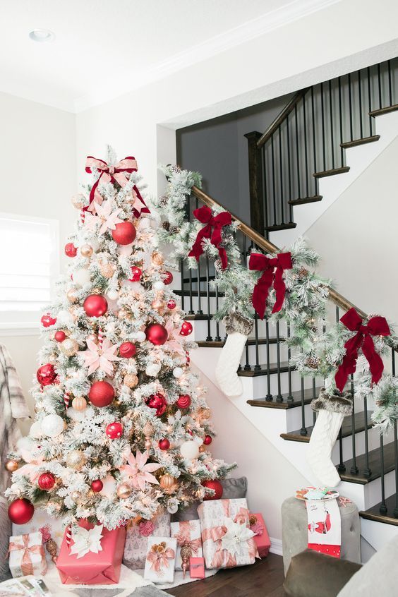 a flocked Christmas tree with red, metallic and white ornaments of various sizes and lights plus snowy greenery and red bows