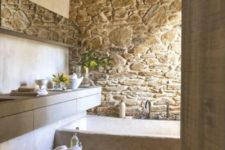 11 a neutral famrhouse bathroom with a stone wall and a neutral stone bathtub plus wooden beams