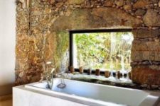 12 a rough stone wall with a window and a tub placed next to it to make an accent and a statement