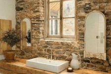 13 a rustic bathroom with a stone accent wall, a rough wooden slab vanity and some greenery and mirrors