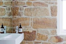 14 a rustic chic bathroom with a rough stone wall with neutral grout and a wooden stool that are an amazing combo