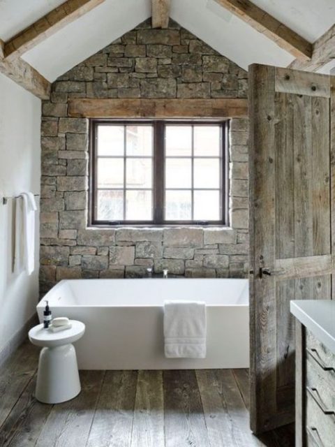 a stylish modern cabin bathroom with a stone wall, wooden beams on the ceiling and a wooden floor looks super inviting