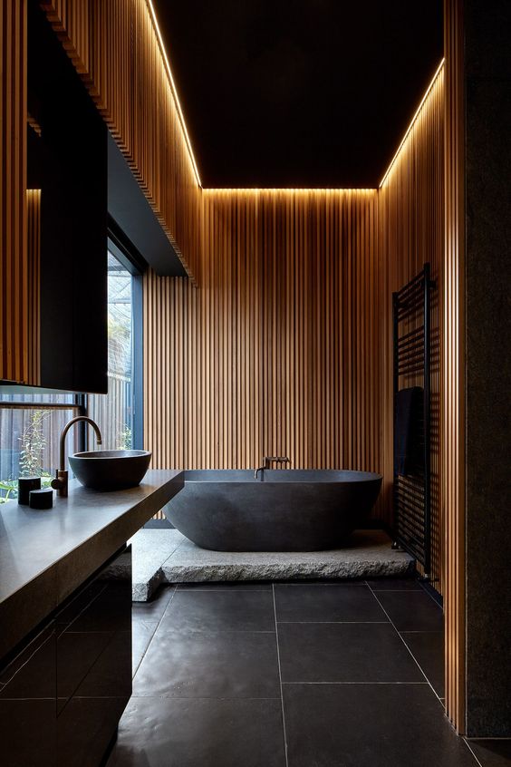 a minimalist contrasting bathroom with sleek wooden slab walls, a rough stone platform and a sleek stone bathtub
