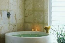 22 a spiritual bathroom nook done with stone-like tiles and a sleek stone round bathtub