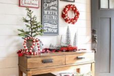 a Christmas console table with pompom garlands and wreaths, evergreens, ornaments and a tree in a bucket