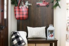 a Christmas sign, an evergreen garland with pinecones and berries, plaid decor and a lantern
