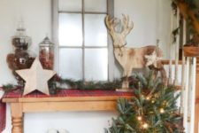 a Christmas tree with lights in a crate, an evergreen garland with berries, a plaid runner and a plywood deer