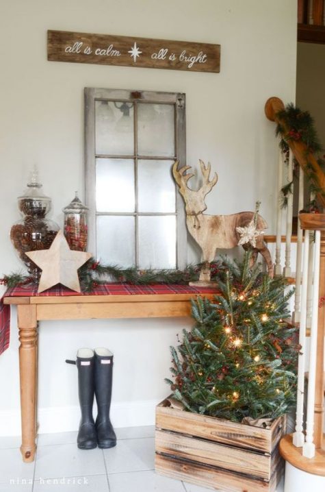 a Christmas tree with lights in a crate, an evergreen garland with berries, a plaid runner and a plywood deer