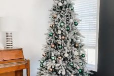 a beautiful flocked Christmas tree decorated with white, copper and green ornaments and a green chair for the holidays