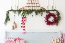 a berry wreath, gift boxes, an evergreen garland, candles and vintage bells for a Christmas entryway