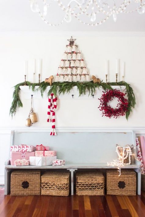 a berry wreath, gift boxes, an evergreen garland, candles and vintage bells for a Christmas entryway