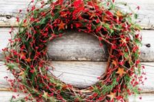 a bold rustic Christmas wreath with stars cut of ornages, lots of berries, greenery and evergreens