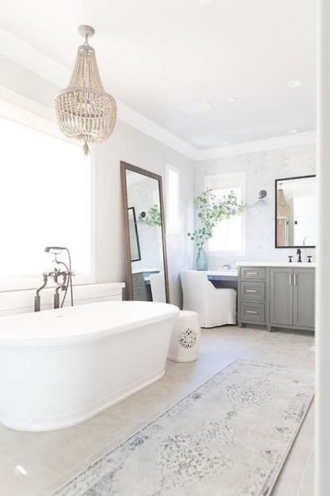 a chic farmhouse bathroom with a grey vanity, a printed rug, a wooden bead chandelier and a large mirror