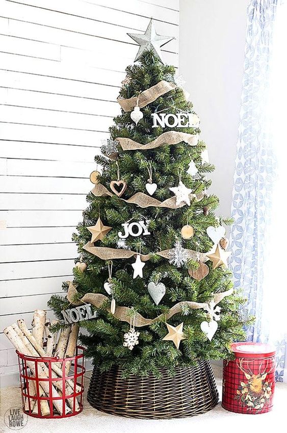 a cool rustic christmas tree decorated with burlap ribbons, wooden stars and slices, with firewood in a bucket by its side