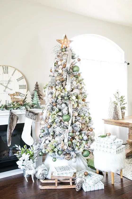 a flocked Christmas tree decorated with green, brown and gold ornaments, ribbons, a marquee light star on top and some leaves