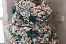 a flocked Christmas tree decorated with light and dark green ornaments, butterflies, fabric blooms and silver leaves and twigs