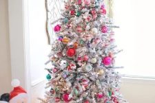 a flocked Christmas tree decorated with red, pink, green, yellow and silver ornaments of various sizes and shapes and spruced up with lights