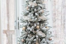a flocked Christmas tree decorated with white and gold ornaments, with white ribbon, placed in a basket for a farmhouse feel