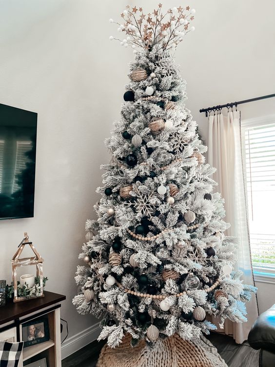 a flocked Christmas tree with metallic and black ornaments, snowflakes, wooden beads and branches on top
