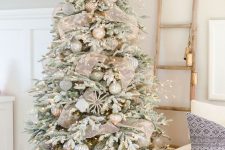 a glam flocked Christmas tree with mush ribbon, metallic and white ornaments and lights is a catchy and chic decoration