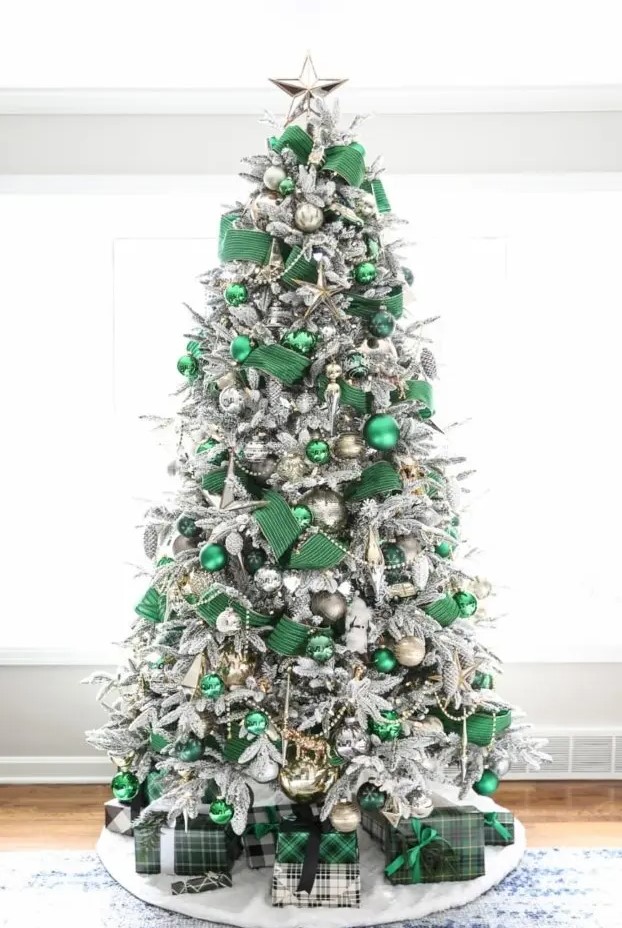 A jaw dropping flocked Christmas tree styled with emerald ribbons and ornaments, gold and silver ornaments and beads and a silver star tree topper